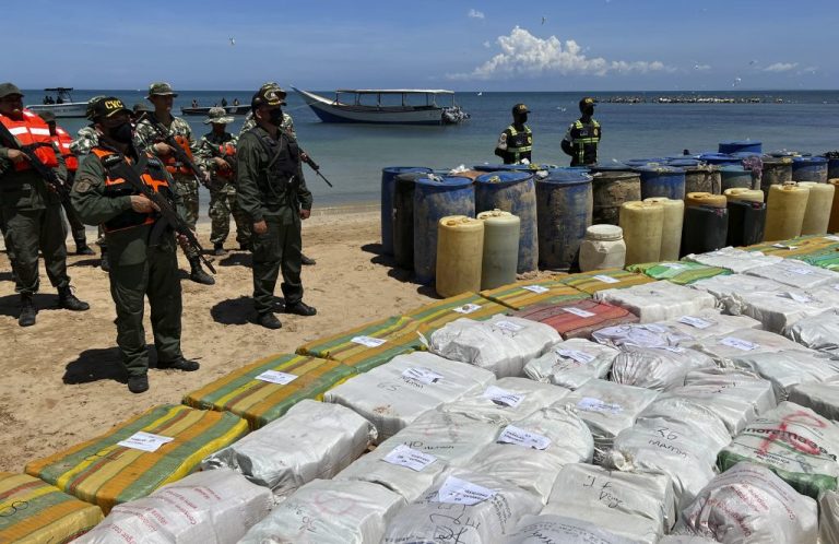 Sacks containing illegal drugs and plastic barrels containing fuel are displayed at a beachside campsite.