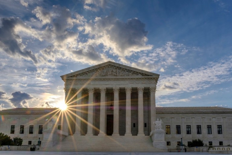 The sun flares in the camera lens as it rises behind the Supreme Court.