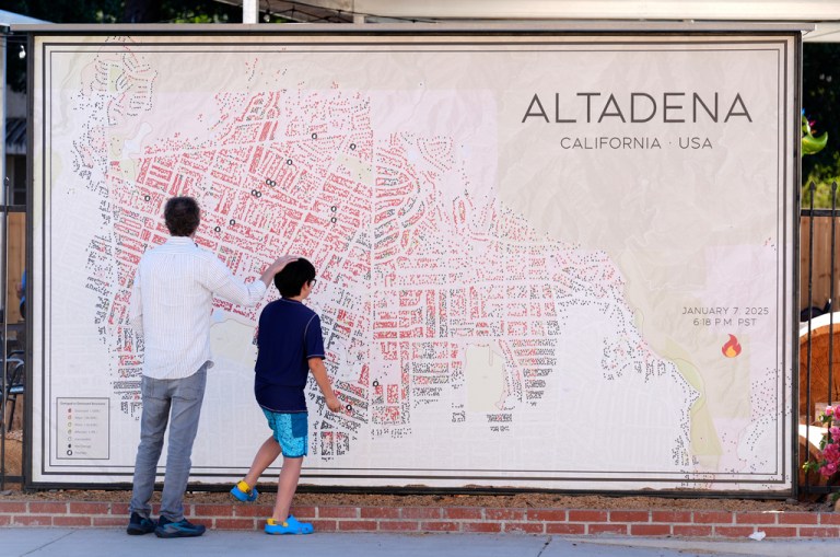 Sam Holtzman and his son Eibu, 9, residents of northwest Altadena, whose house still stands but remains inaccessible due to Eaton Fire contamination in January, look at a map of Altadena fire damage created by Noel McCarthy, a stylized update of Los Angeles County's Eaton Fire damage map,