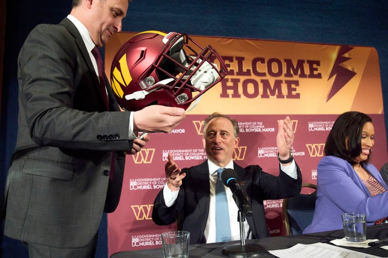 Washington Commanders controlling owner Josh Harris is passed a helmet to sign.