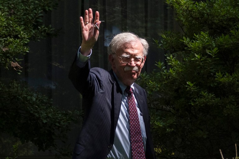 Former national security adviser John Bolton waves as he arrives at his house.