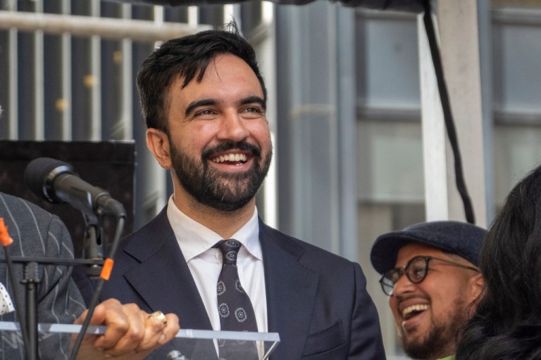 Zohran Mamdani smiles behind a podium