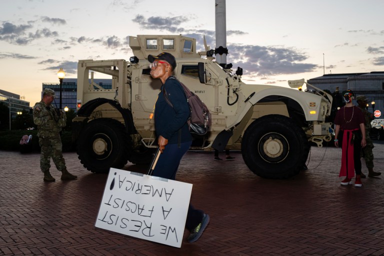 A protester walks past members of the D.C. National Guard and a Mine Resistant Ambush Protected vehicle at Union Station.