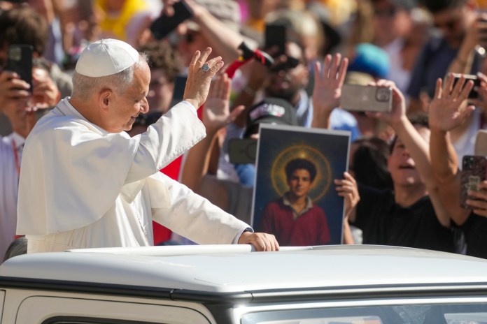 Pope Leo XIV waves to faithful holding a picture of Blessed Carlo Acutis, who will be canonized Sunday, as he arrives in St. Peter's Square at the Vatican for an open-air jubilarian audience Saturday, Sept. 6, 2025.