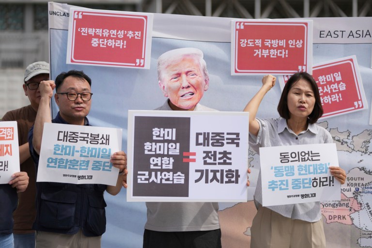 A protester wearing a mask of U.S. President Donald Trump and others shout slogans during a press conference to oppose the military exercise called Freedom Edge near the U.S. Embassy in Seoul, South Korea, Monday, Sept. 15, 2025. The part of letters read 
