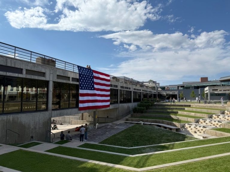 People gaze down at the site where Charlie Kirk was shot, above which hangs an American flag, at Utah Valley University.