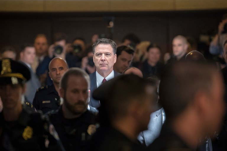 Former FBI Director James Comey stands in hallway.