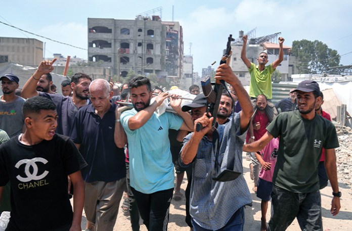 A man fires a weapon as Palestinians carry the bodies of people who were killed in an Israeli airstrike on a school in Gaza that has been used as a shelter, during their funeral near the Al Shifa Hospital in Gaza City on July 25. (AFP via Getty Images)