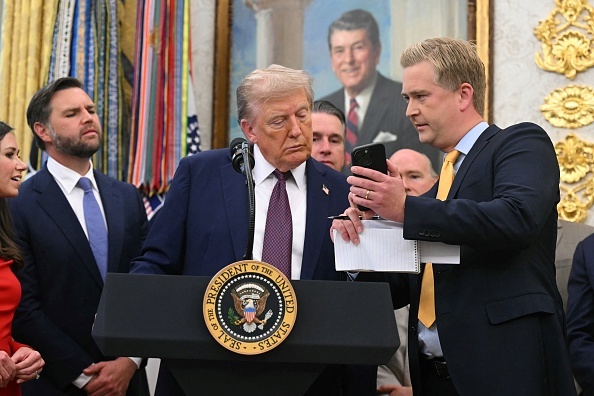 Fox News reporter Peter Doocy shows President Donald Trump his phone as he makes an announcement in the Oval Office.