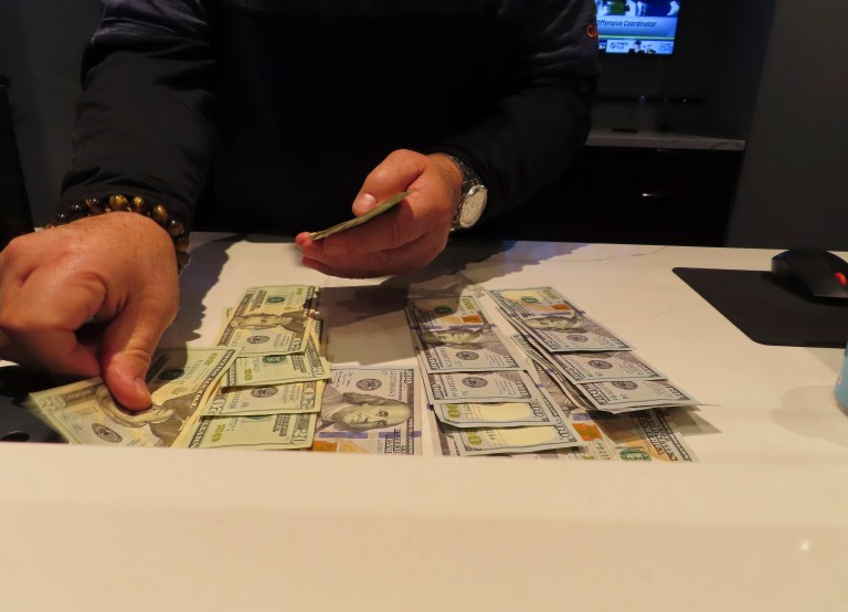 A worker counts money on a counter.