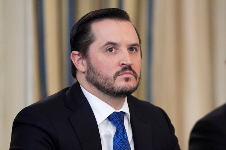 Taylor Budowich, dressed on in a suit, looks at something.