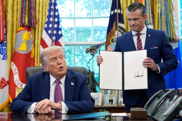 Pete Hegseth holds up an executive order while standing next to President Trump in the Oval Office