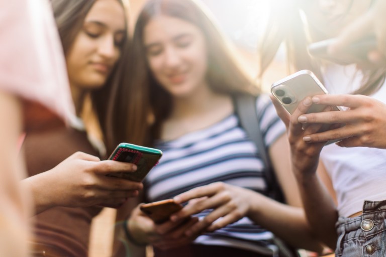 Group of teenage students standing in schoolyard and using mobile phones. They are very happy and playful.