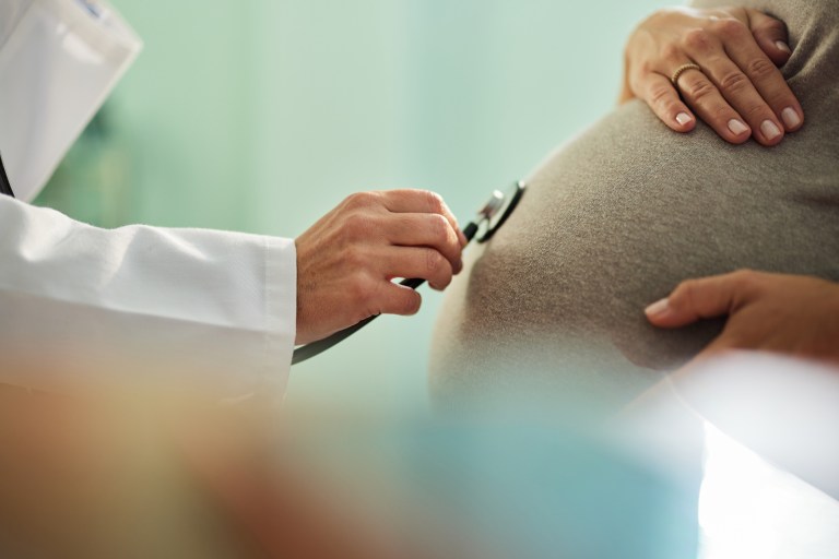 Close up of a doctor's hand using stethoscope to listen to a baby's heartbeat of a pregnant woman.