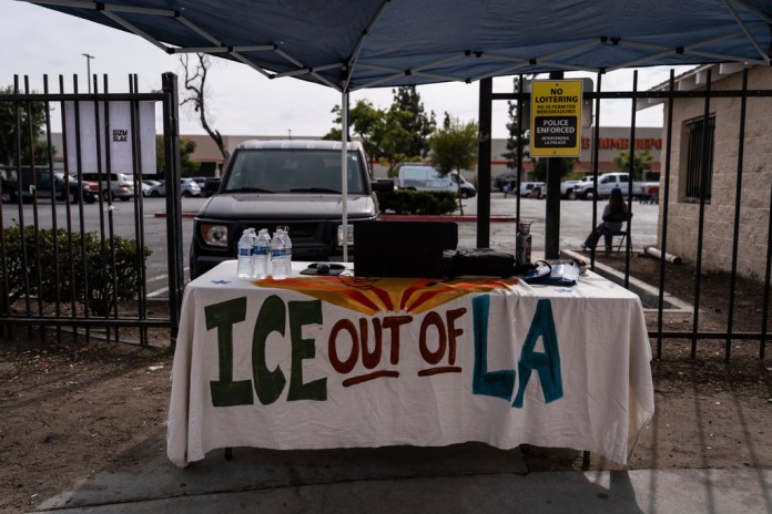 A table covered with a cloth reading "ICE Out of LA" sits under a canopy next to the job center for day laborers outside a Home Depot.