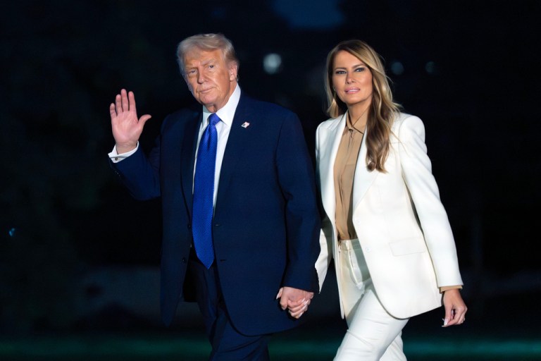 President Donald Trump waves to media while holding hands with first lady Melania Trump.