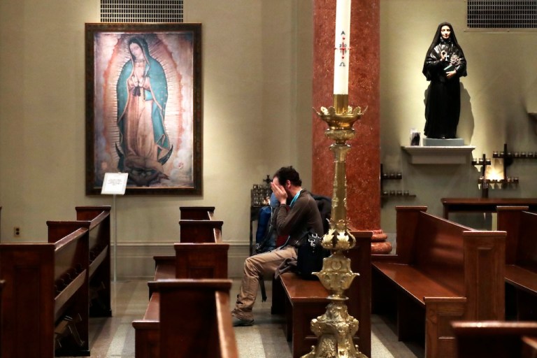 A man sits alone in a pew at St. James Cathedral, the Cathedral for the Catholic Archdiocese of Seattle, in an otherwise nearly empty sanctuary.