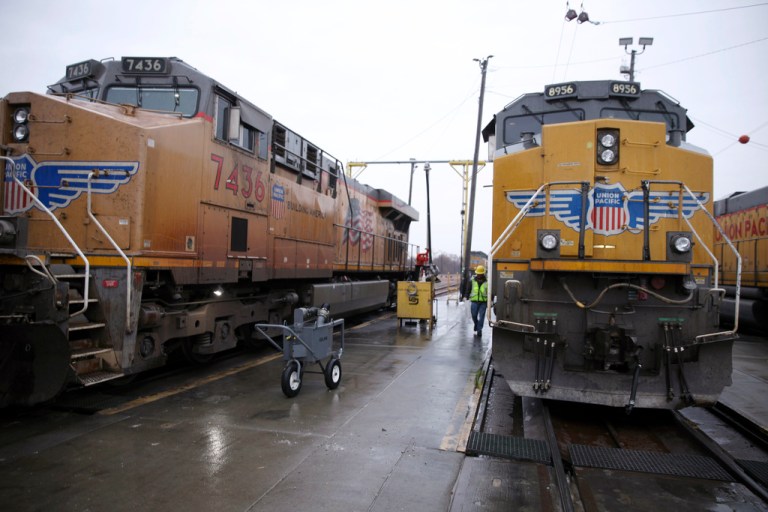 A Union Pacific worker walks between two locomotives that are being serviced in a railyard in Council Bluffs, Iowa, on Dec. 15, 2023. Recent layoffs at Union Pacific and BNSF, combined with an investment fund's campaign to take control of Norfolk Southern, are renewing concern among unions and regulators about how job cuts might affect safety and service. (AP Photo/Josh Funk)