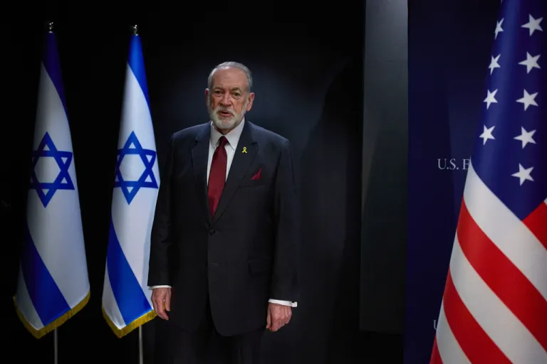 Mike Huckabee stands between the Israeli and American flags.