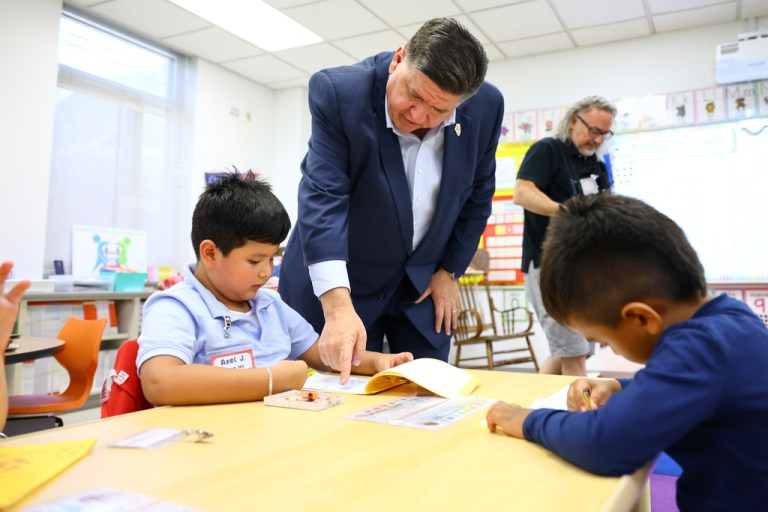 Gov. J.B. Pritzker helps a kindergarten student at Prairie Oak Elementary School in the suburb of Berwyn, Thursday, Sept. 4, 2025, in Chcago, as he visits the school to learn about the impacts of pending federal actions on school communities to families and students.