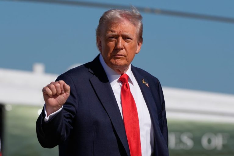 Donald Trump wearing a blue suit, red tie, and holding his fist in the air mid way
