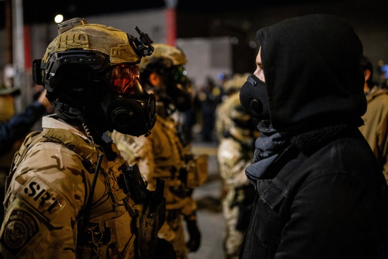 An officer with the Department of Homeland Security Special Response Team (SRT) stands against a protester.