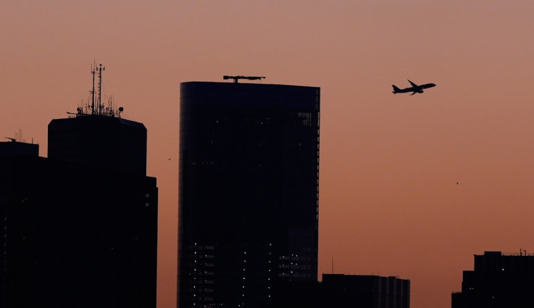 A airplane climbs out from Logan Airport over downtown at dawn, Monday, Oct. 6, 2025, in Boston. (AP Photo/Charles Krupa)