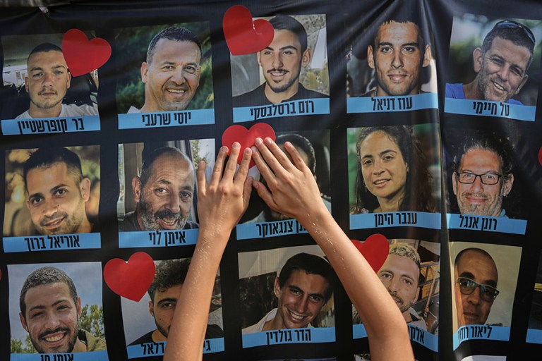 A person pastes a heart-shaped sticker on a banner with pictures of Israeli hostages during a a gathering at a plaza known as hostages square in Tel Aviv, Israel, Monday, Oct. 13, 2025. (AP Photo/Oded Balilty)