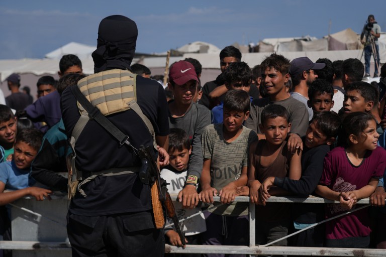 A masked Hamas gunman stands as people gather.