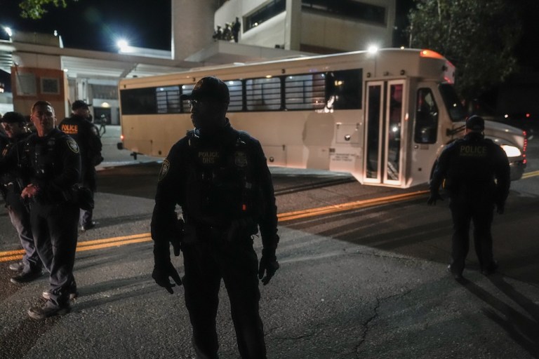 Law enforcement officers line the road outside an Immigration and Customs Enforcement facility as a bus leaves with passengers.