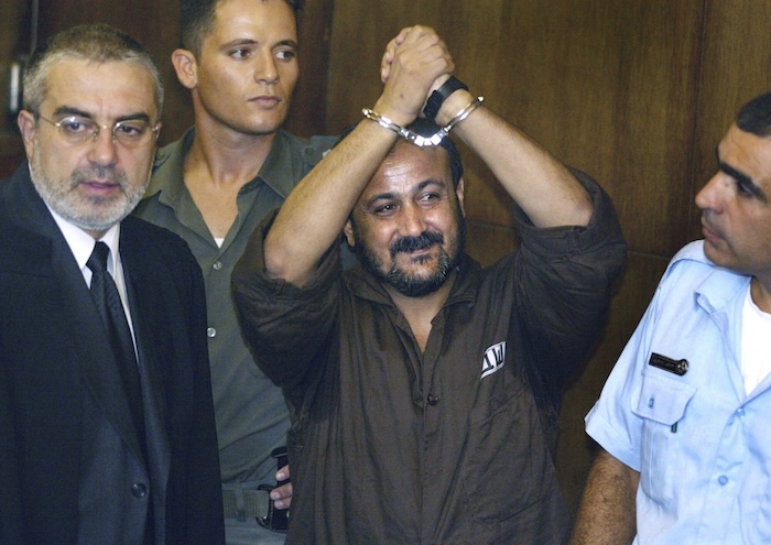 Marwan Barghouti, center, raises his handcuffed hands in the air on the opening day of his trial in Tel Aviv, Israel, Aug. 14, 2002. (AP Photo/Brennan Linsley, File).