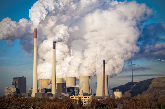 Smoke rises from a U.S. coal plant with wind turbines in the background.
