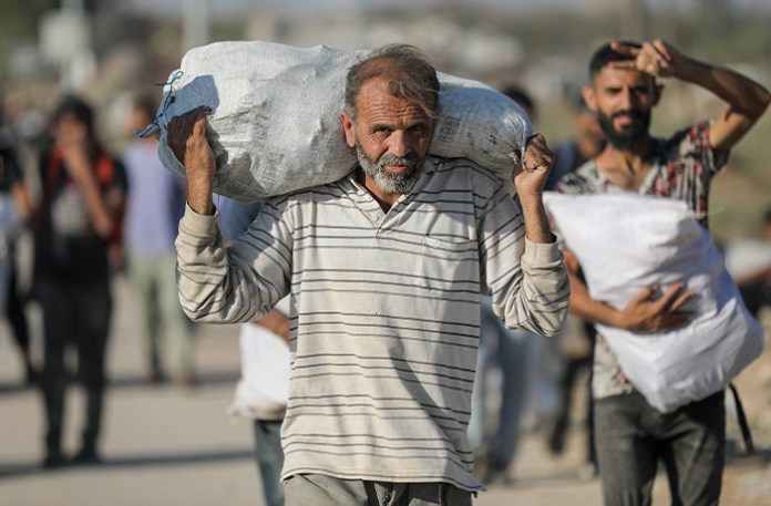Palestinians walk back through the Netzarim corridor in central Gaza carrying aid parcels received from a U.S.-based aid distribution point set up by the privately-run Gaza Humanitarian Foundation on June 26, 2025, amid the humanitarian crisis after 20 months of conflict with Israel. (MOIZ SALHI/Middle East Images/AFP via Getty Images)
