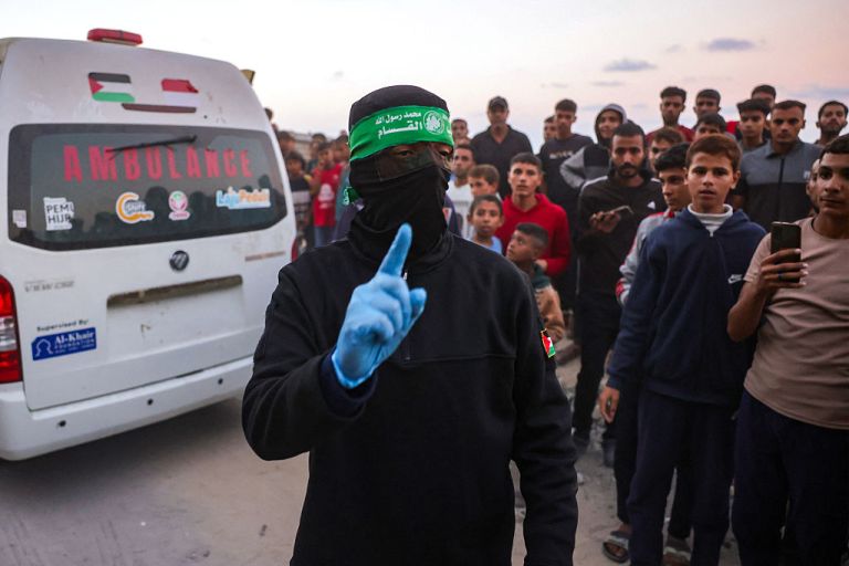 A Hamas militant gestures as people gather around an ambulance carrying a body retrieved from a tunnel in an area north of Khan Yunis in the southern Gaza Strip on October 28, 2025. Israel's military on October 28 accused Hamas of staging its search for the remains of a Gaza hostage body, one of 28 the group had agreed to hand over under a ceasefire deal. Hamas says it is committed to the ceasefire terms, but lacks the equipment needed to locate and excavate hostage bodies potentially buried under buildings collapsed by air strikes. (Photo by Bashar TALEB / AFP) (Photo by BASHAR TALEB/AFP via Getty Images)