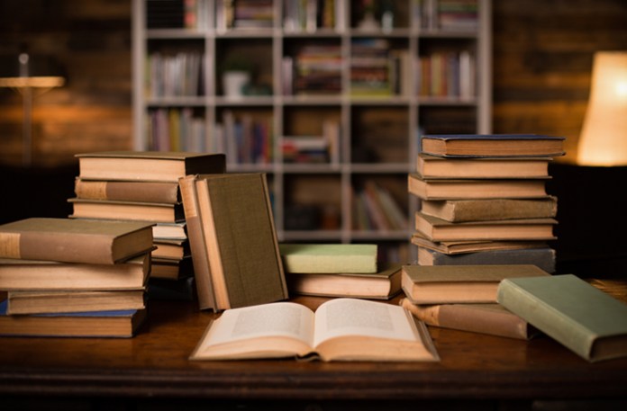 Books on a desk with book shelves in the background.
