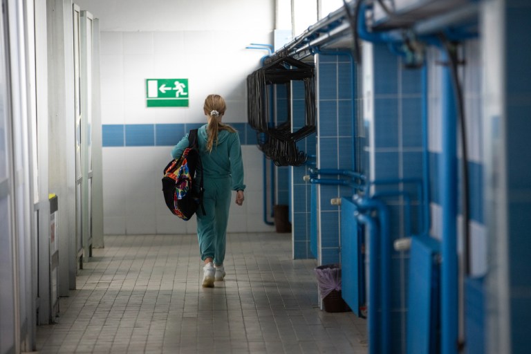 Girl with backpack leaving after swimming practice in public swimming pool.