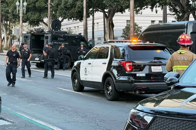 Law enforcement walk around police cars after a man crashed into City Hall.