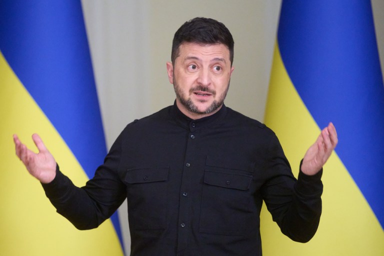 Zelensky talks during a press conference in front of Ukrainian flags.
