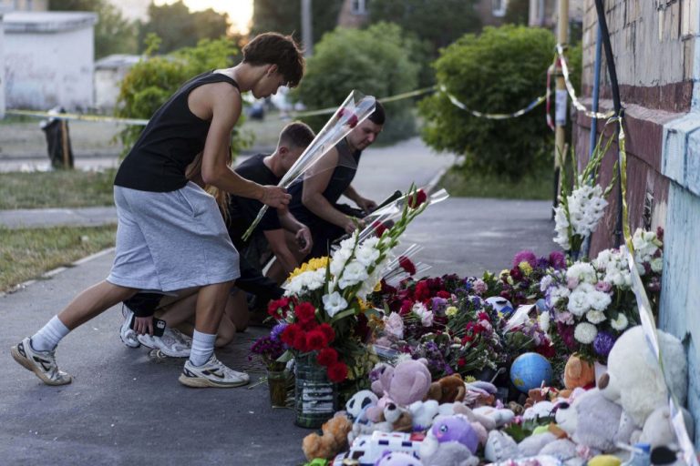 Children put flowers on a site of a house that was destroyed by a Russian strike.