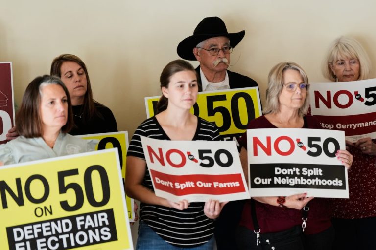People hold up signs opposing Prop 50 during a press conference in Chico, Calif., Wednesday, Oct. 29, 2025. (AP Photo/Godofredo A. Vásquez)