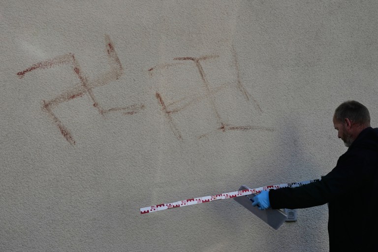 Criminal experts measure swatsikas at a house in Hanau, Germany, Thursday, Nov. 6, 2025, the day after a a person painted with blood swastikas on cars and houses.