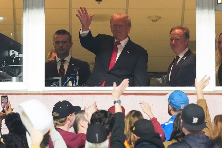 Trump waves at a crowd from the box of a stadium