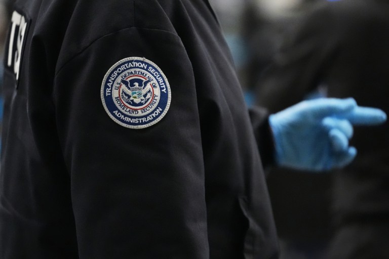 A TSA employee wears a jacket with the TSA and Department of Homeland Security logo.