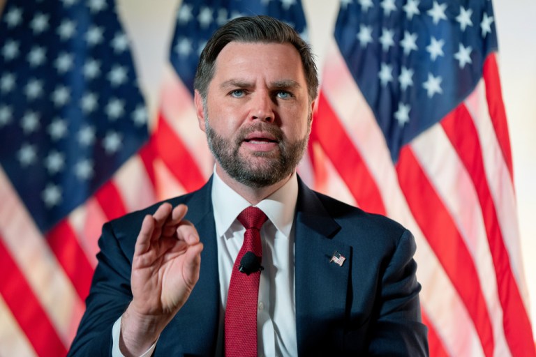Vice President JD Vance gestures as he speaks in front of American flags.