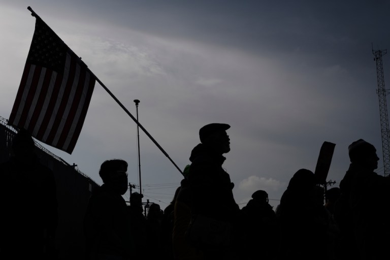 Silhouetted protesters walk outside, with one holding a flag.