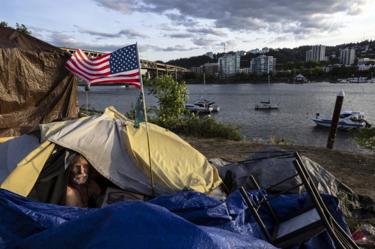 Frank, a homeless man sits in his tent with a river view in Portland, Ore., Saturday, June 5, 2021. The city council in Portland, Oregon, has approved new homeless camping rules. Under the rules, people who reject offers of shelter can face penalties, including fines of up to $100 or up to seven days in jail.