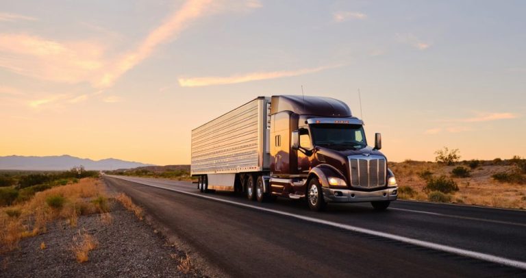 A large semitruck hauls freight on an open highway under a morning sky.