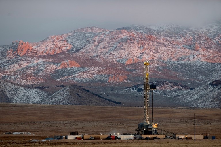 A drill rig at a geothermal site with mountains in the background.