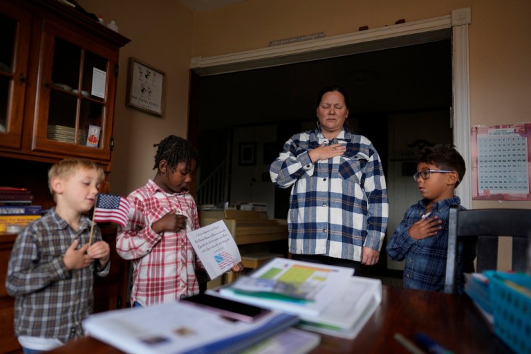 With hands over their hearts, Erin Young and her three adopted children from left, Isaac, 5, Gianna, 7, and Lucas, 8, say the Pledge of Allegiance as they begin their homeschooling lessons, Tuesday, Nov. 12, 2024, in Sunbury, Ohio.