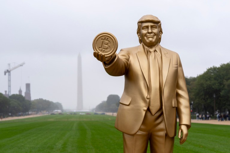 A statue of President Donald Trump holding a bitcoin in recognition of his support for cryptocurrency is displayed on the National Mall with the Washington Monument behind.
